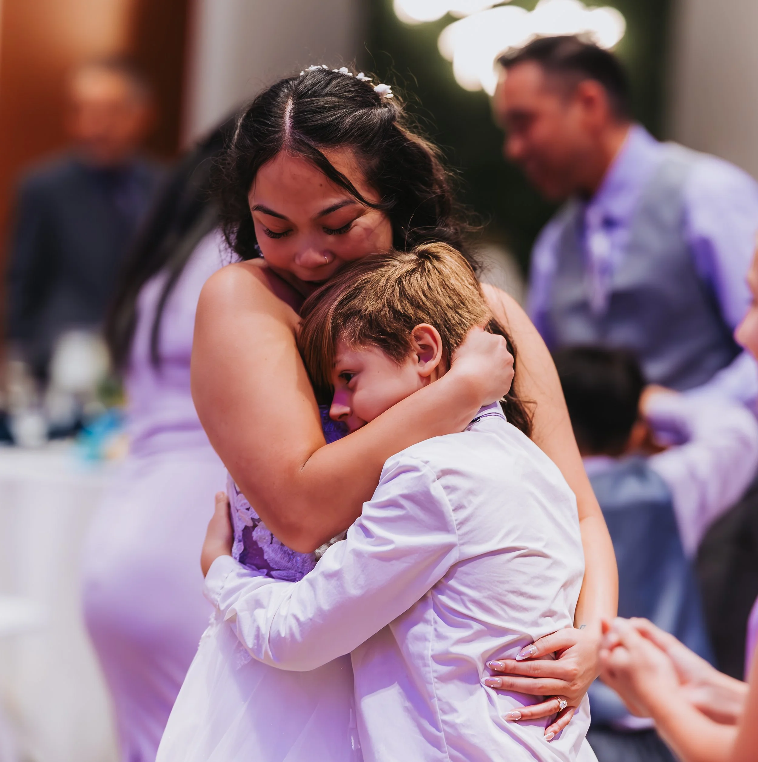 A woman hugging a young boy at a celebration, with people in formal attire in the background. western wedding photographer az rustic wedding photographer az barn wedding photographer az backyard wedding photographer az