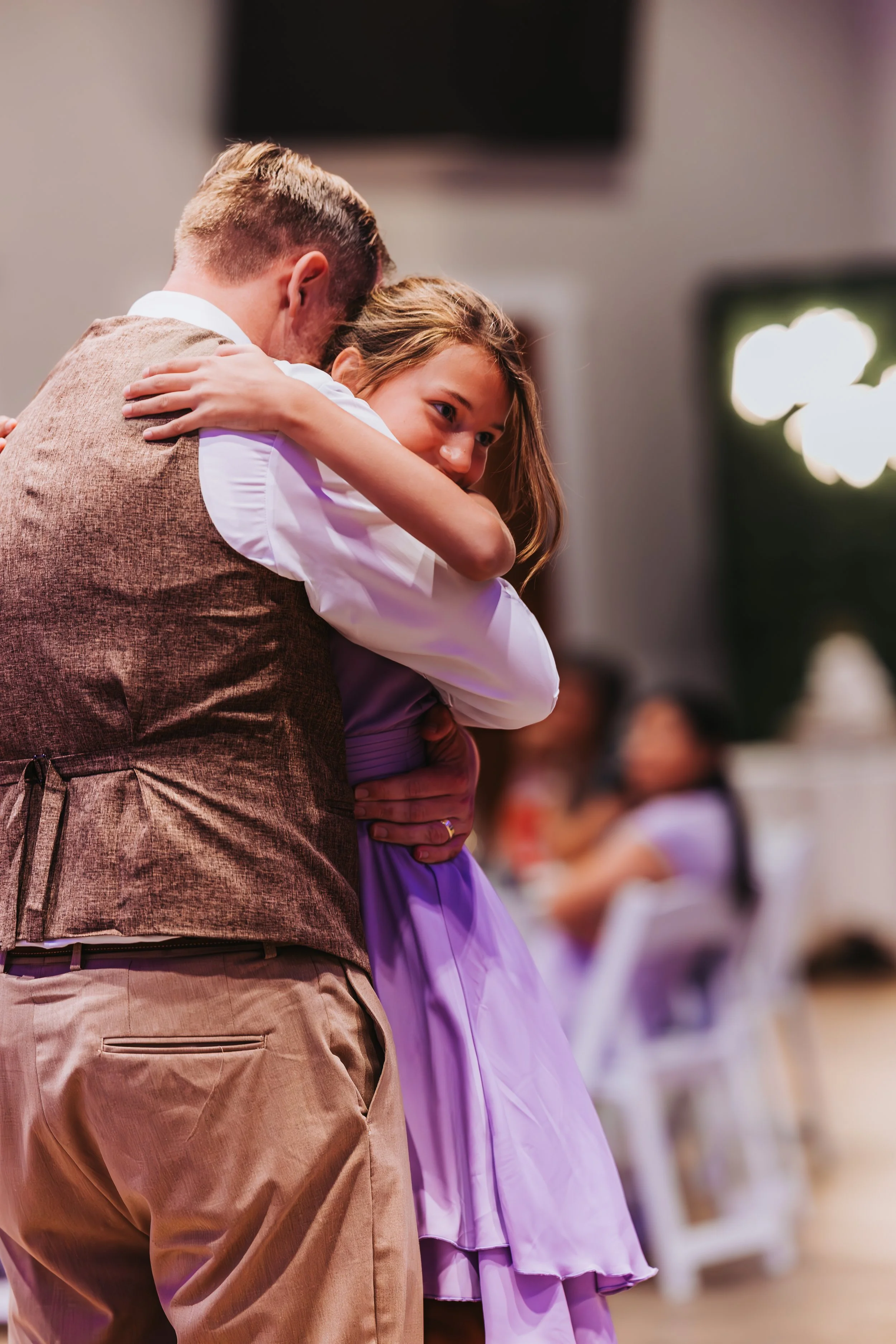A young girl with a smile embraces a man, possibly her father, during a celebration or dance event indoors. western wedding photographer az rustic wedding photographer az barn wedding photographer az backyard wedding photographer az