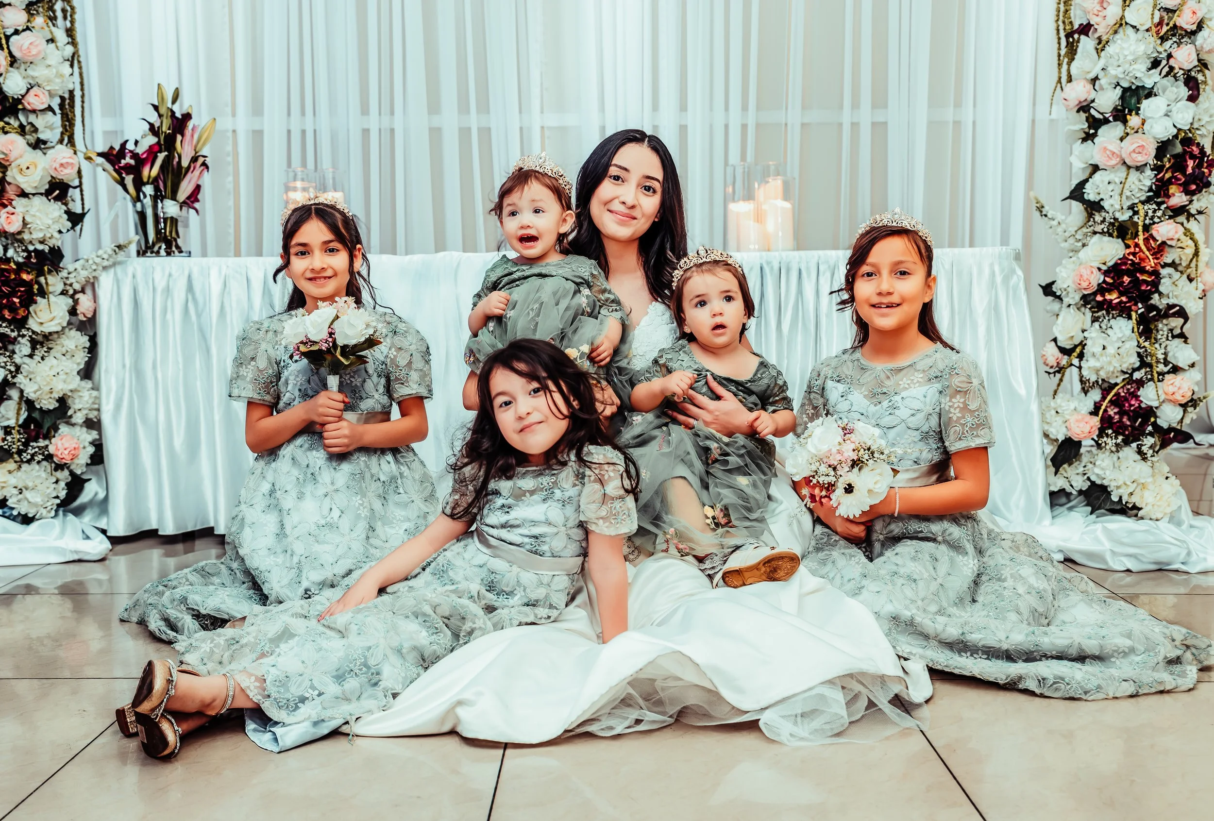 A woman and five young girls dressed in pastel dresses at a celebration with floral decor and candles. indoor Mexican wedding photographer phoenix az