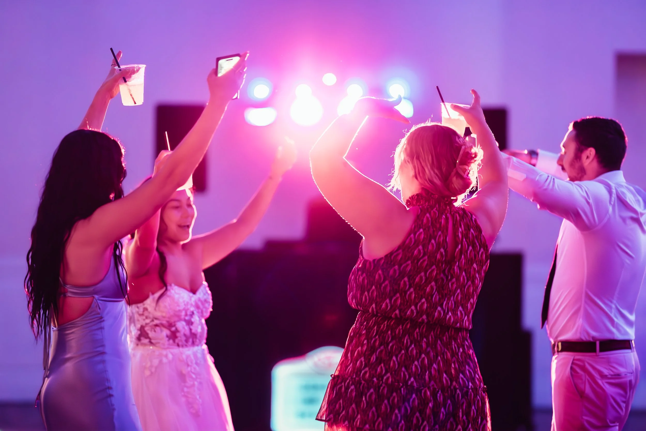 Group of people dancing and enjoying drinks at a party with vibrant pink and purple lighting. western wedding photographer az rustic wedding photographer az barn wedding photographer az backyard wedding photographer az