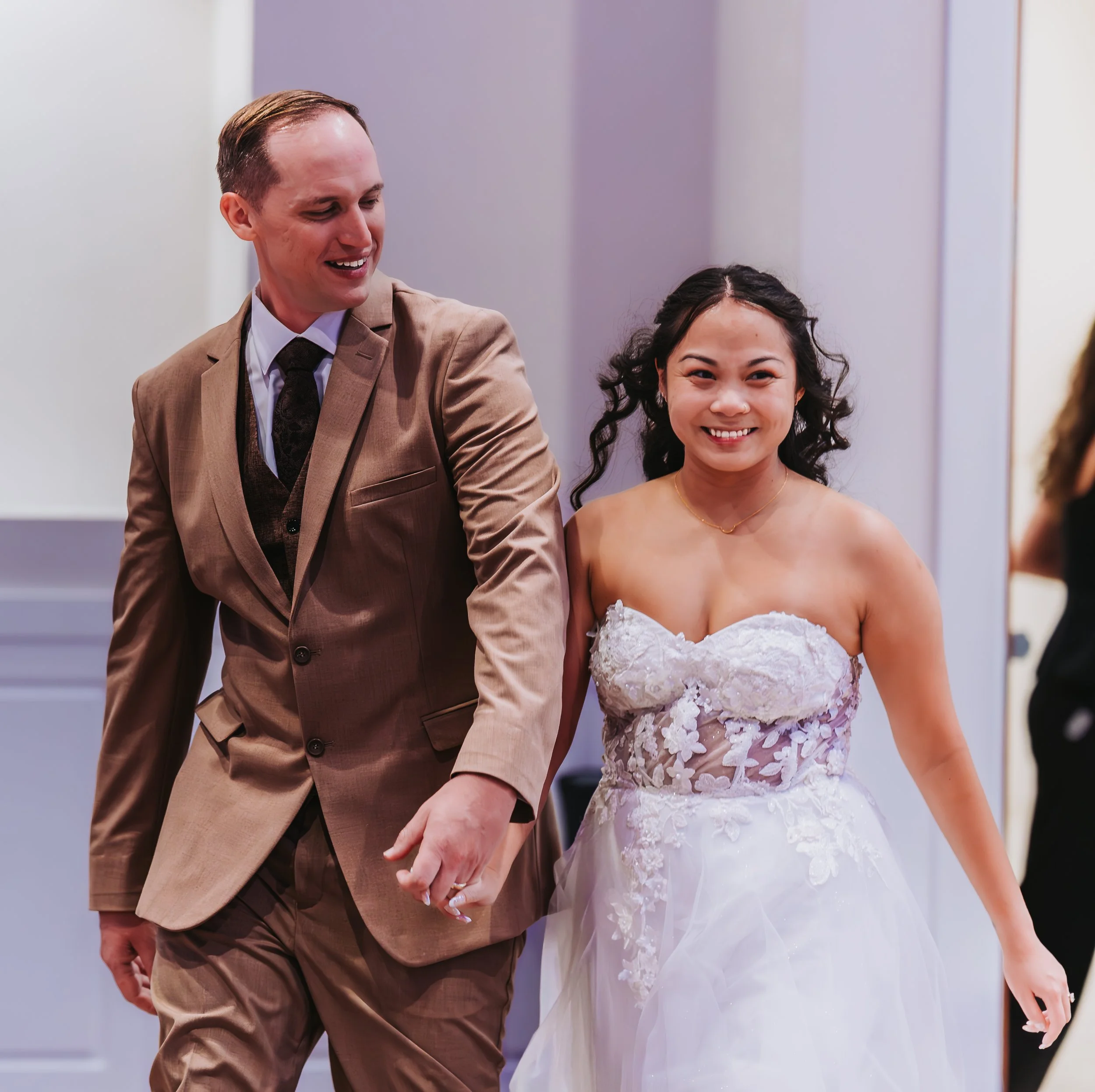 A smiling bride in a white wedding dress holding hands with a groom in a brown suit at a wedding reception. engagement wedding photographer phoenix az engagement photographer az traveling wedding photographer az