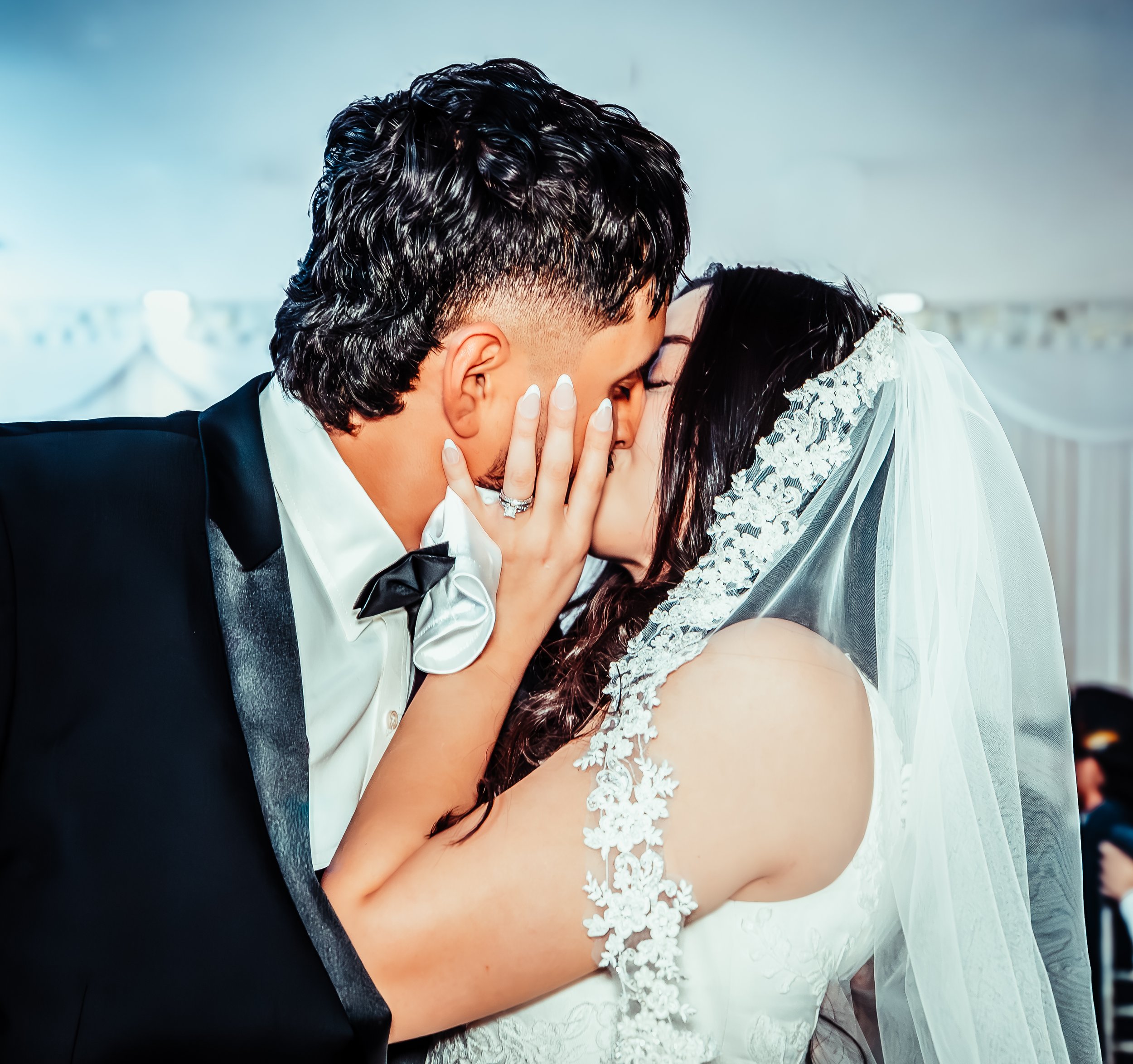 A bride and groom sharing a kiss at their wedding with the bride wearing a veil and lace dress, and the groom in a tuxedo. indoor Mexican wedding photographer phoenix az