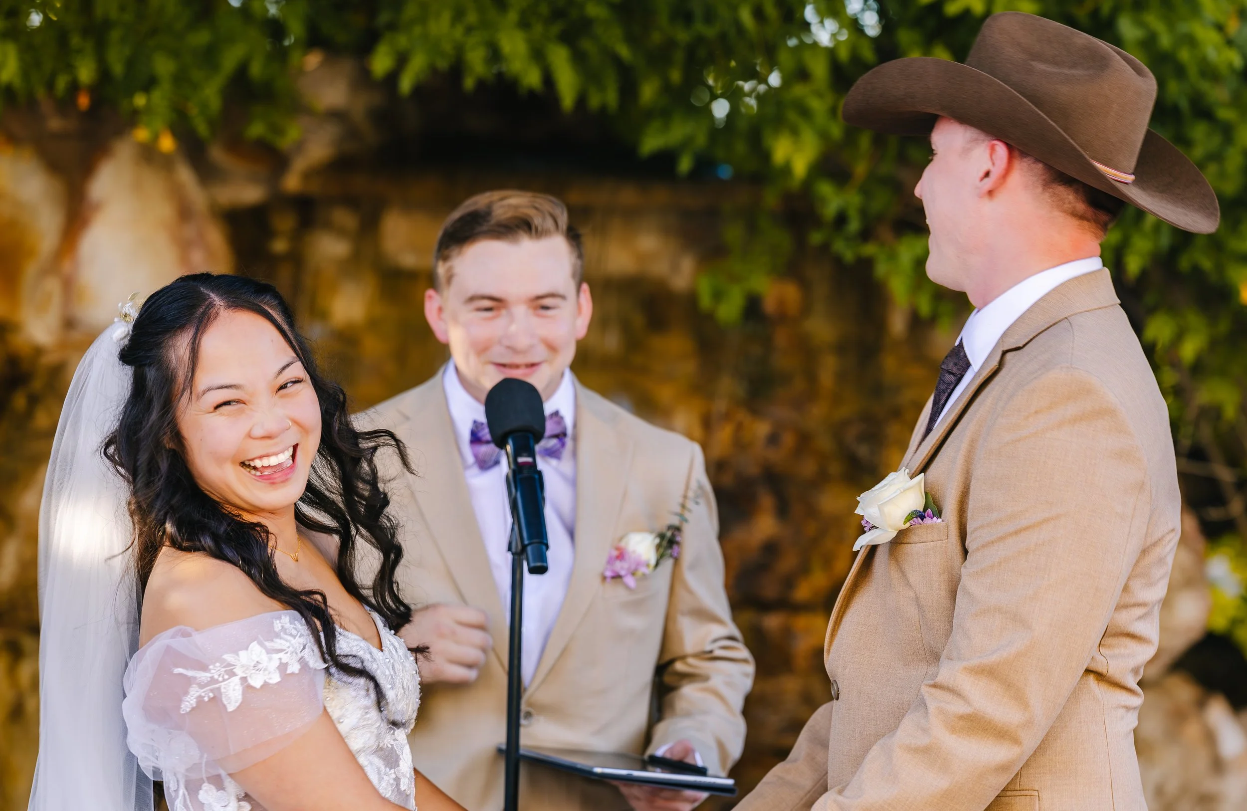 A wedding ceremony outdoors with the bride laughing and the groom smiling as they exchange vows, with an officiant reading from a small black book. traveling wedding photographer az wedding photographer Prescott az wedding photographer flagstaff az