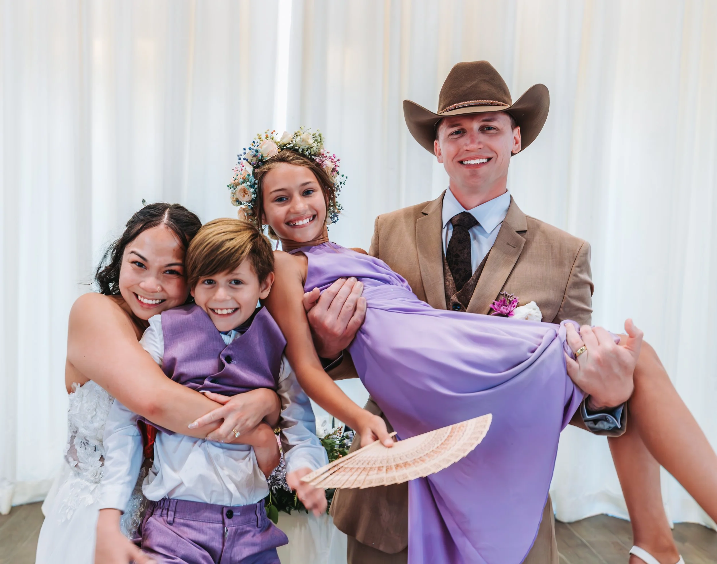 A man in a cowboy hat and beige suit holding a smiling young girl in a purple dress, surrounded by three children at a celebration. engagement wedding photographer phoenix az engagement photographer az traveling wedding photographer az