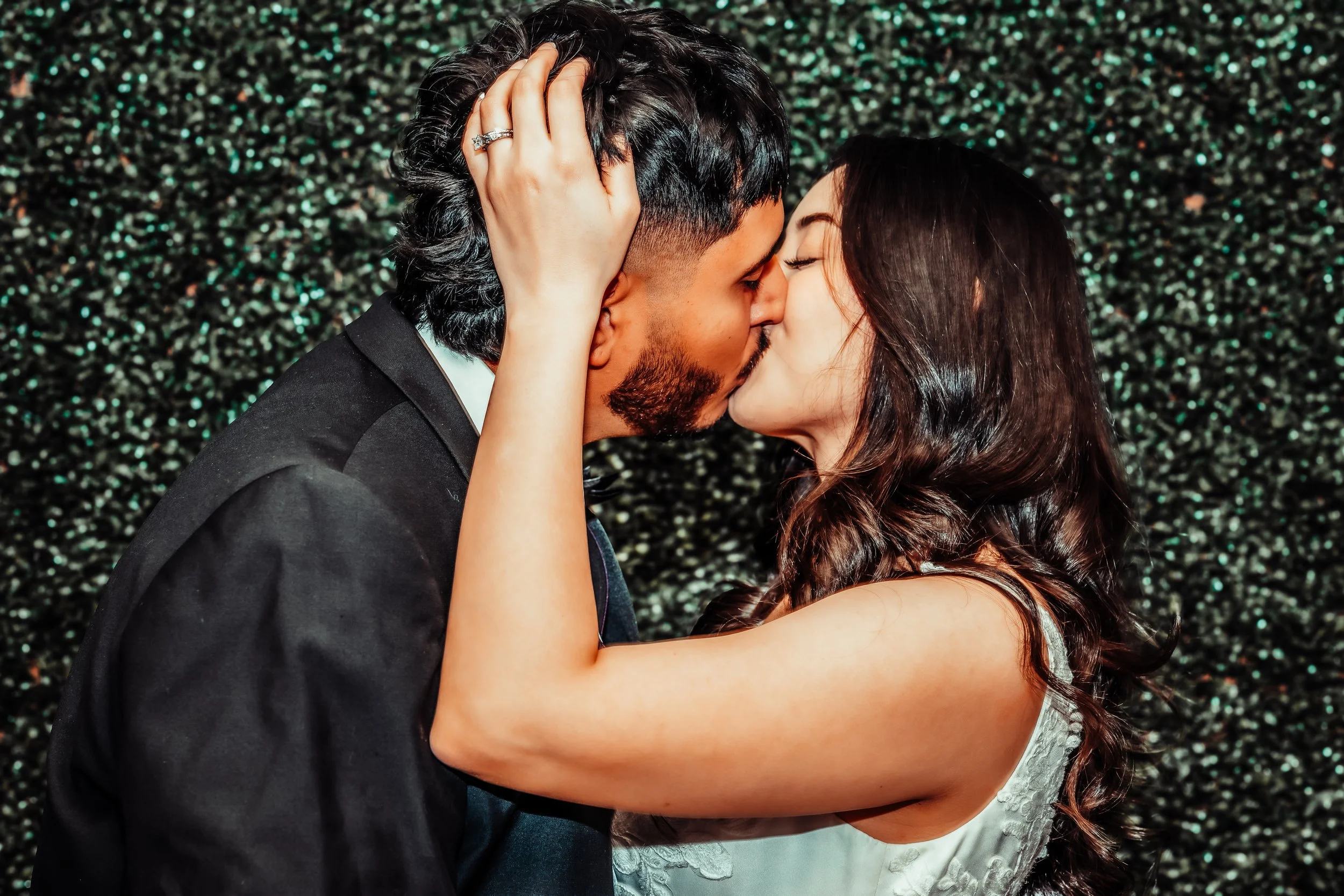 A couple sharing a kiss, with the woman holding the man's head and both with their eyes closed. The woman has dark, wavy hair and wears a white dress. indoor Mexican wedding photographer phoenix az