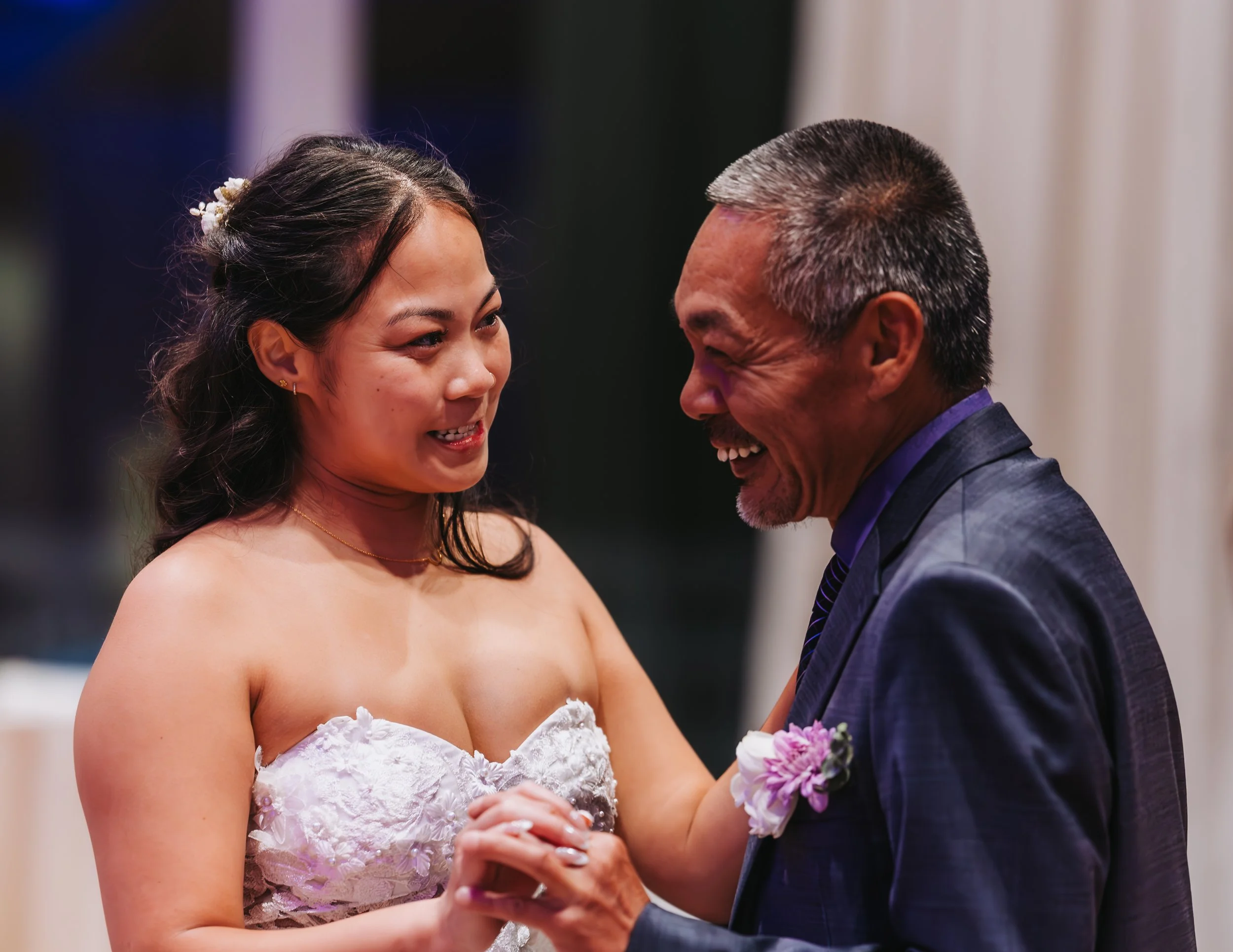A young woman in a white lace wedding dress holding hands with an older man in a dark suit, both smiling during a dance at a wedding reception. western wedding photographer az rustic wedding photographer az barn wedding photographer az backyard weddi