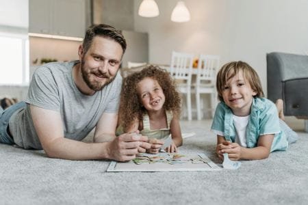 man lying on floor with two children working on puzzle