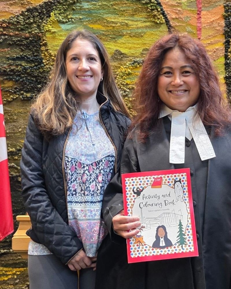 Mildred Peñaranda of Mil & Co. with Hon. Yvonne Clarke, Speaker of the Yukon Legislative Assembly, holding the Activity and Colouring Book illustrated by Mil & Co.