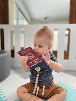 Bebé sosteniendo un pasaporte mientras está sentado sobre una alfombra.