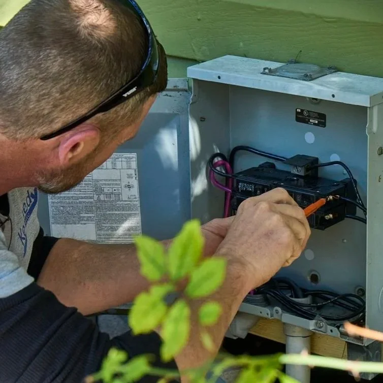 Technician checking exterior electrical panel connections to prevent failures, improve safety, and support reliable power before Florida summer conditions arrive.