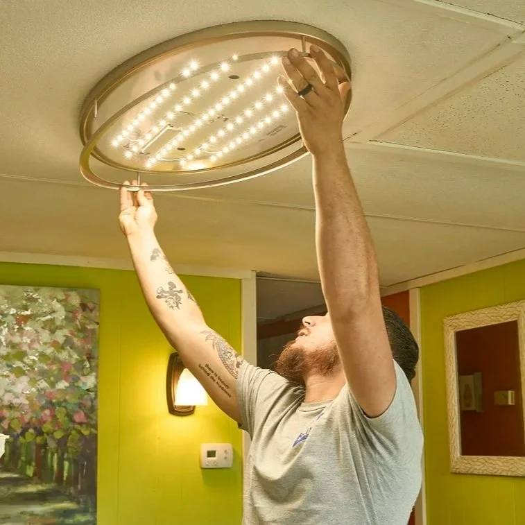 Technician working on LED ceiling fixture representing bedroom electrical use, seasonal comfort devices, and household electrical safety awareness.
