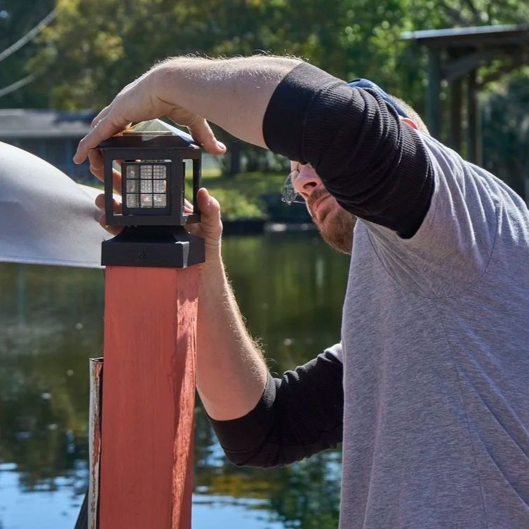 Technician securing exterior light on deck post to improve visibility, safety, and electrical reliability during Florida fall storm season conditions.