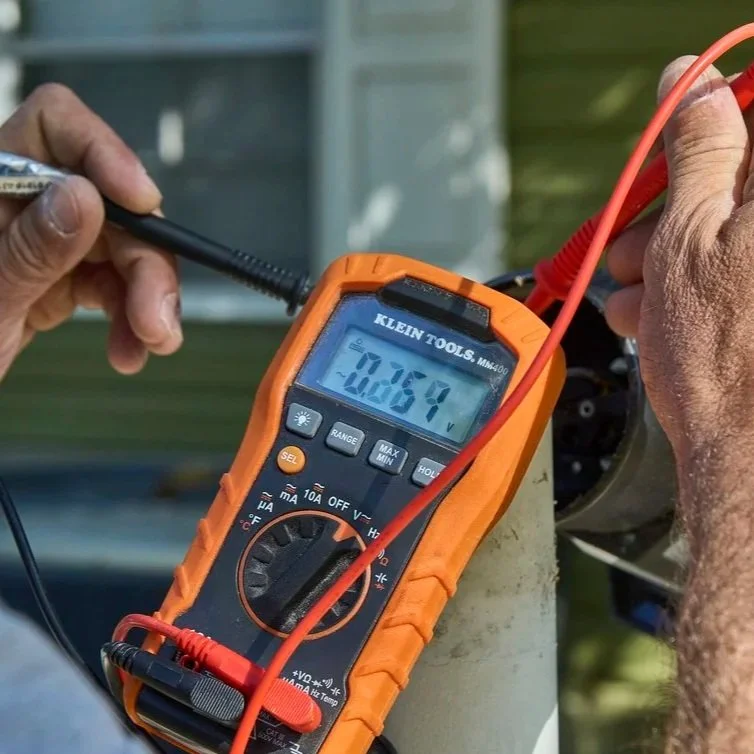 Technician using multimeter to measure circuit demand, illustrating electrical evaluation when choosing between electric and gas dryers.