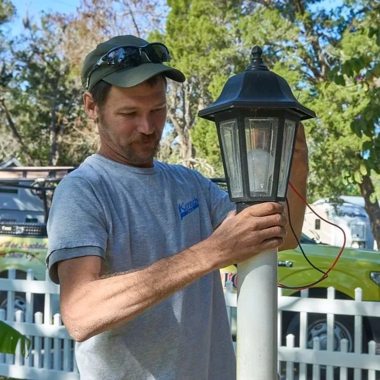 Electrician working on exterior light wiring representing residential electrical load changes, seasonal appliance use, and home safety awareness.