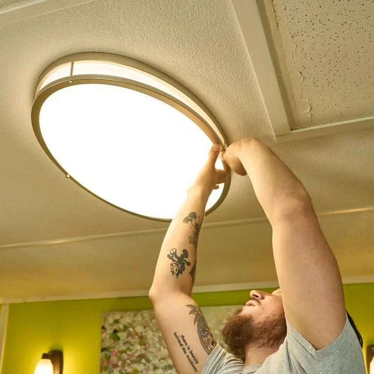 Technician mounting modern ceiling light fixture illustrating household electrical load management and how appliance faults impact circuit stability over time.