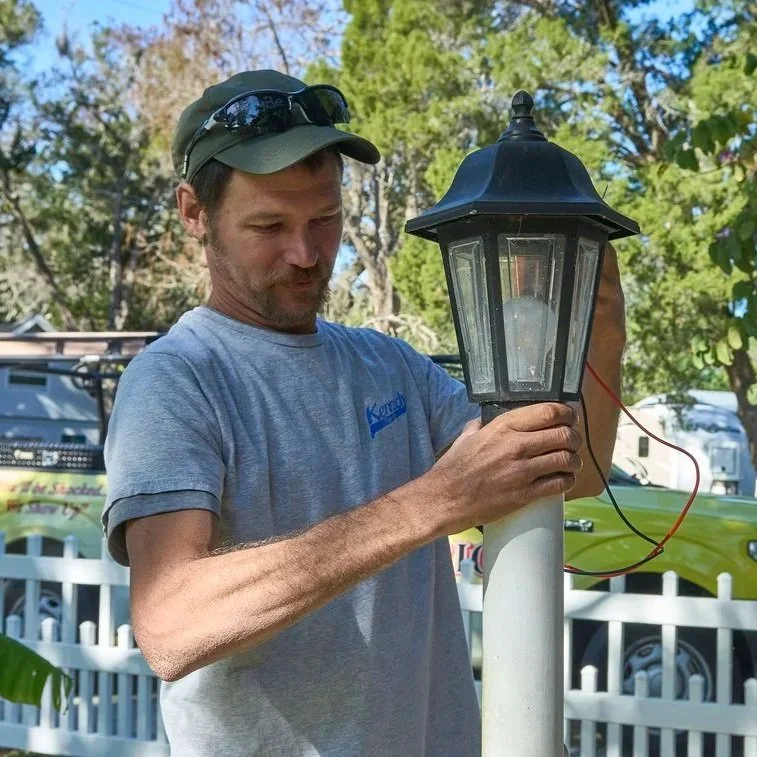 Technician connecting colored electrical wires inside outdoor lamp post fixture to maintain proper grounding, neutral return, and safe power delivery.