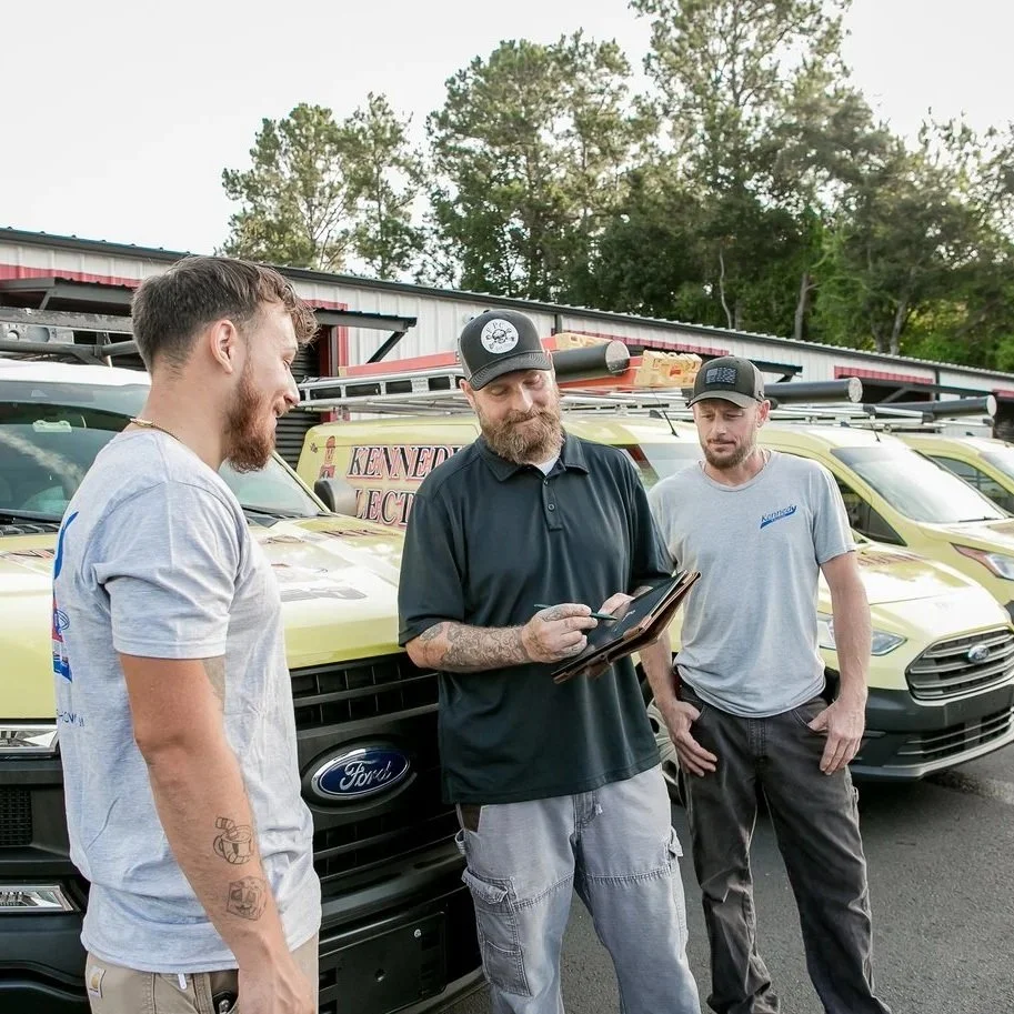 Electricians discussing tablet near service vans, representing professional home EV charging station installation and reliable Florida electrical service.