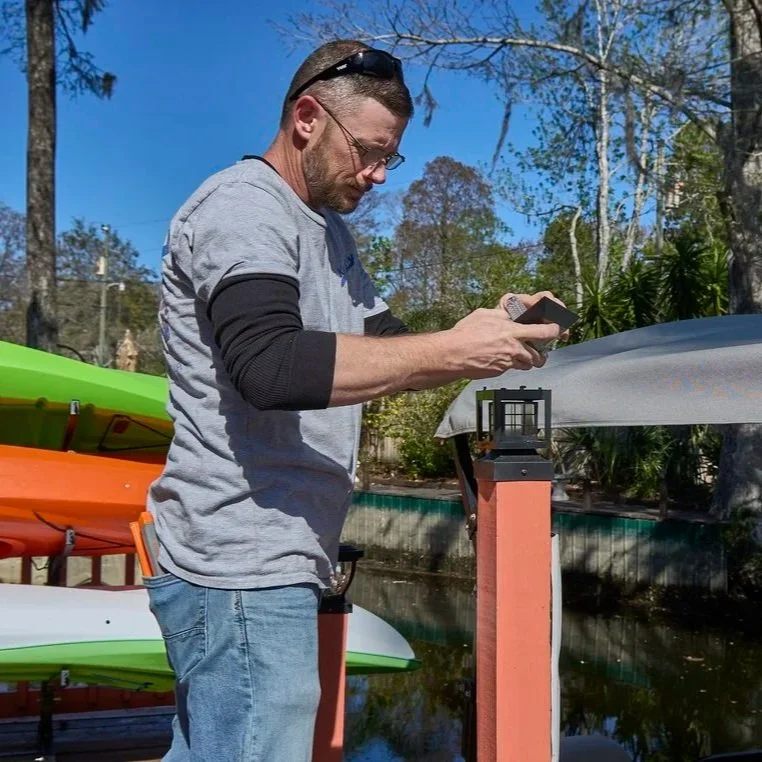 Professional electrician adjusting exterior light post near water, focusing on safe wiring, illumination, and outdoor electrical reliability for families.