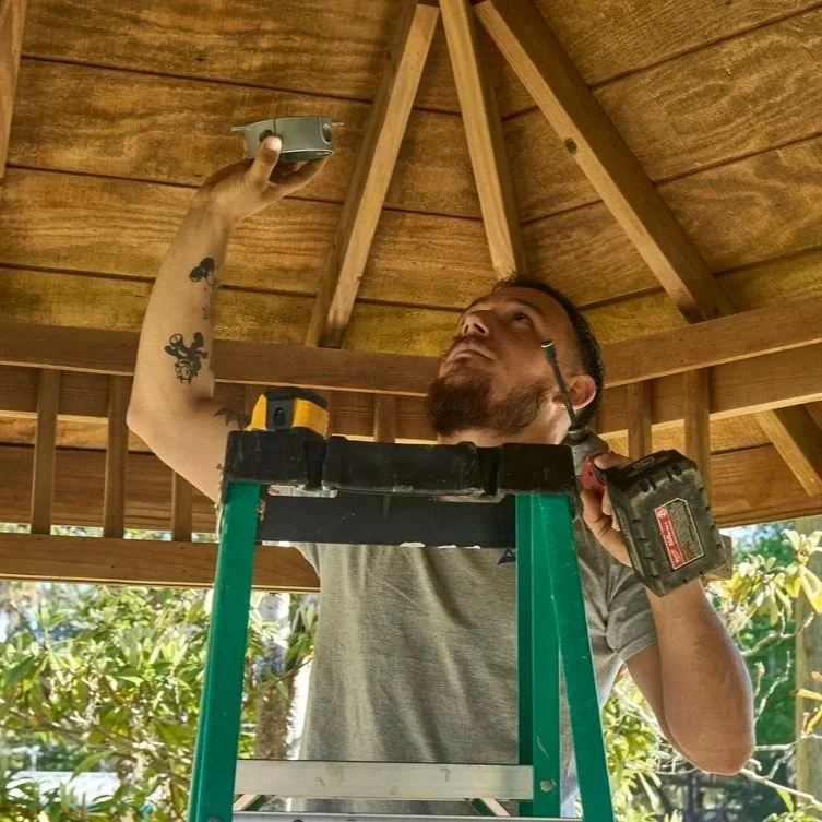 Technician wiring exterior ceiling light on patio, representing home electrical evaluation to identify hidden appliance energy usage and rising costs.