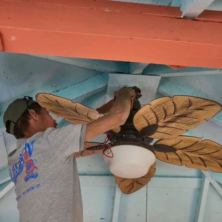 Technician connecting ceiling fan wiring beneath covered porch ceiling, ensuring proper installation, airflow performance, and safe electrical connections.