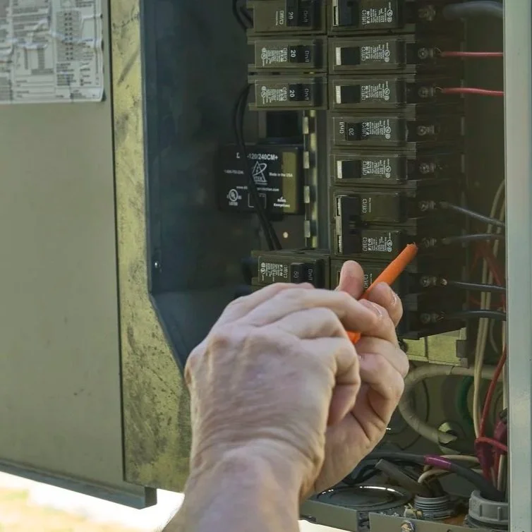 Technician checking outdoor electrical panel near AC system, evaluating circuit load and diagnosing excessive energy consumption from cooling equipment.
