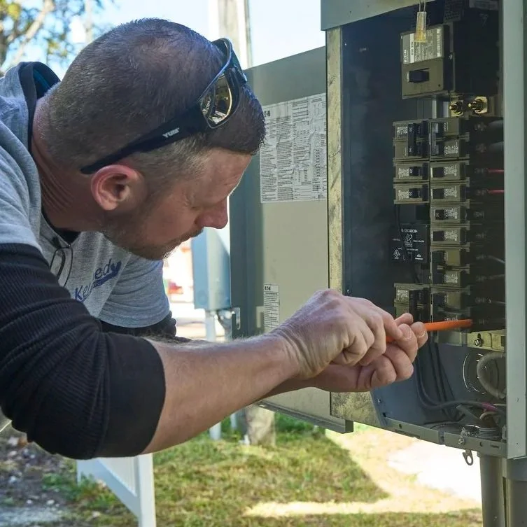 Professional electrician reorganizing panel breakers outdoors, focusing on balanced circuit demand, safer operation, and reliable residential electrical performance.