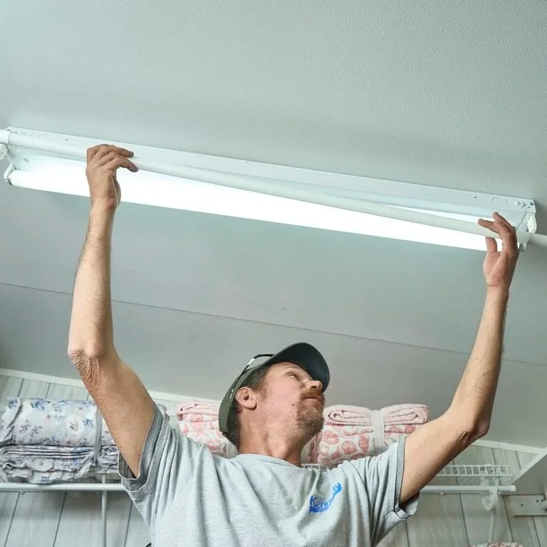 Technician installing ceiling light fixture in laundry room, illustrating appliance maintenance decisions between repair costs, efficiency, and long-term replacement planning.
