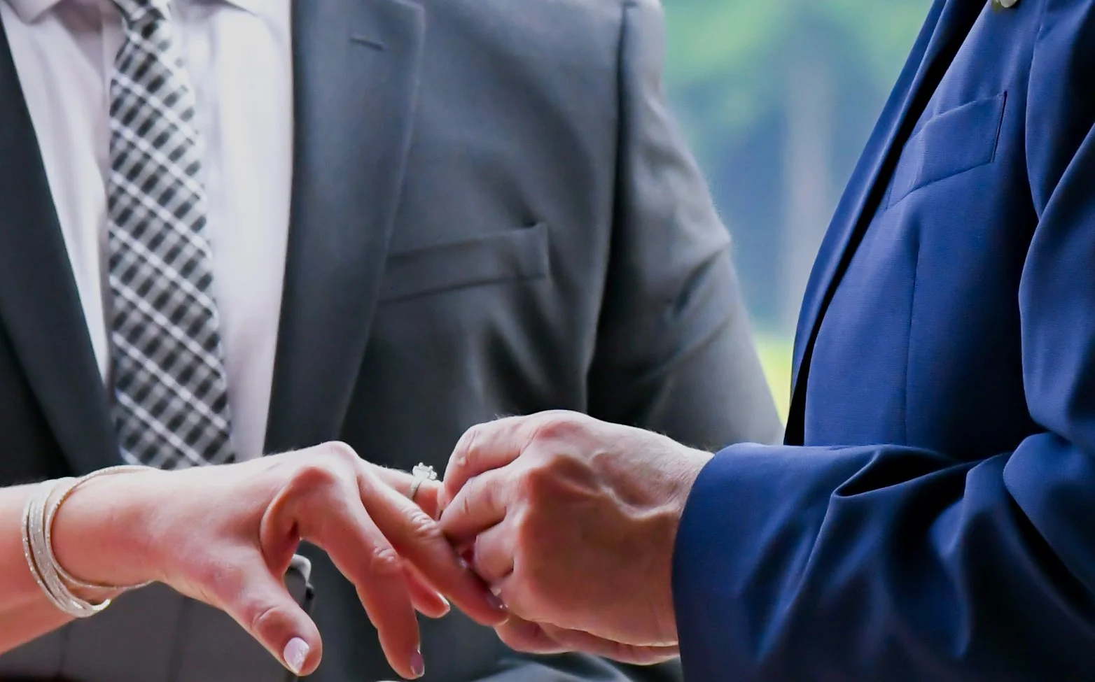 People exchanging wedding rings during a ceremony, with close-up of hands and suits.