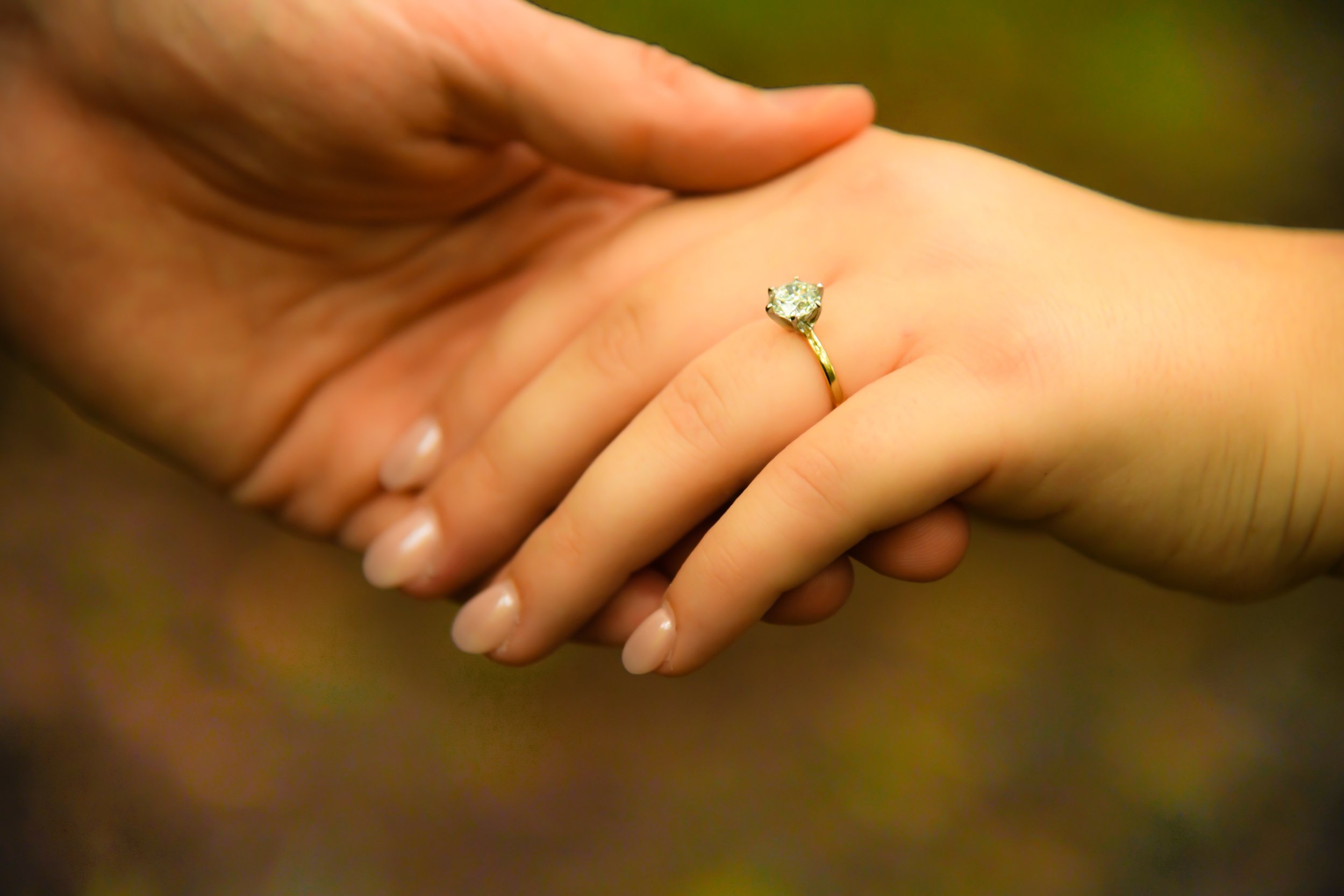 Close-up of two hands gently holding each other, with one hand wearing a gold ring with a diamond.