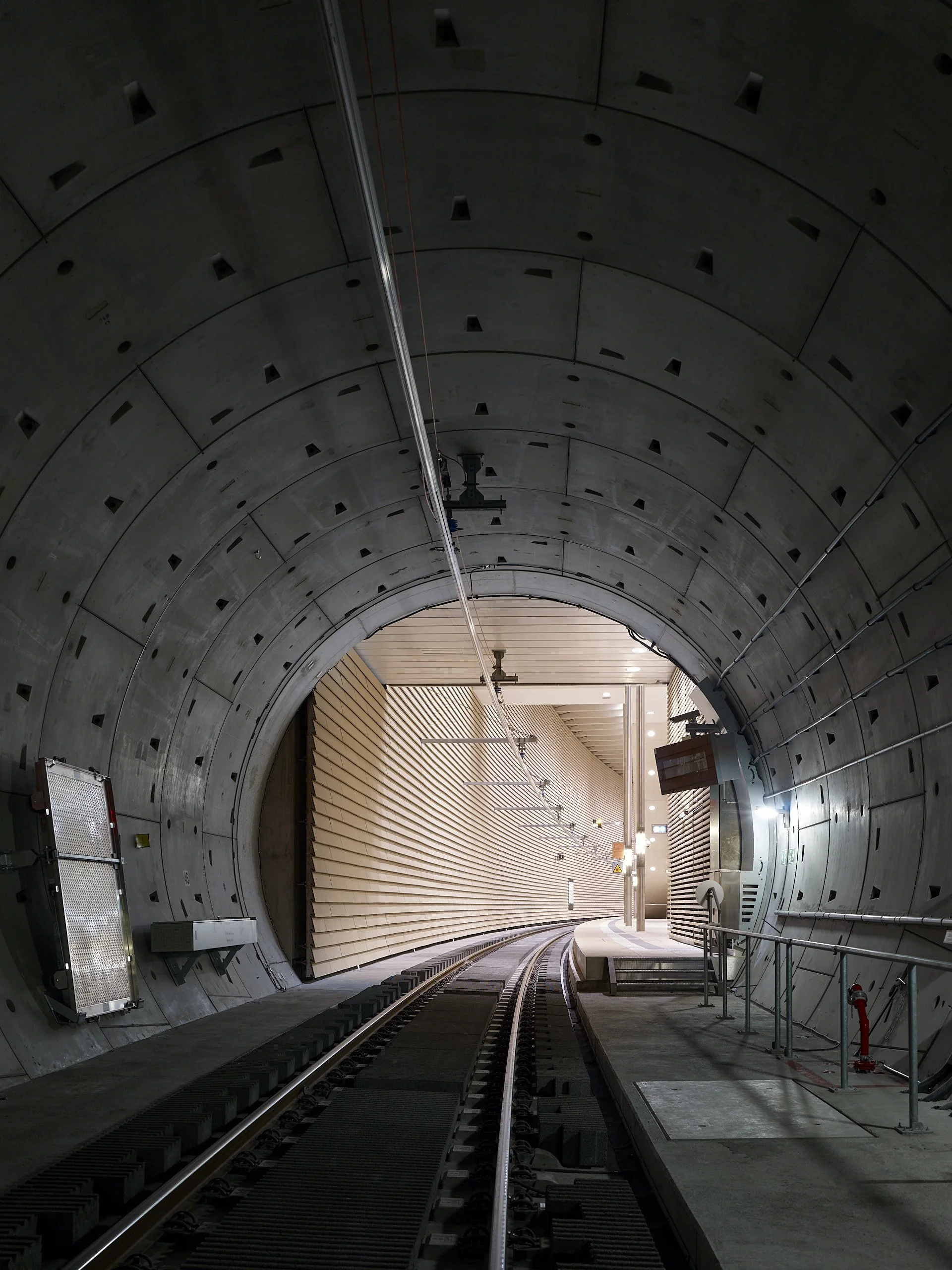 Blick in einen befahrenen Eisenbahntunnel mit Gleisen, Sicht auf die Tunnelwand und die Gleise, die in die helle Ausgangsstelle verlaufen.