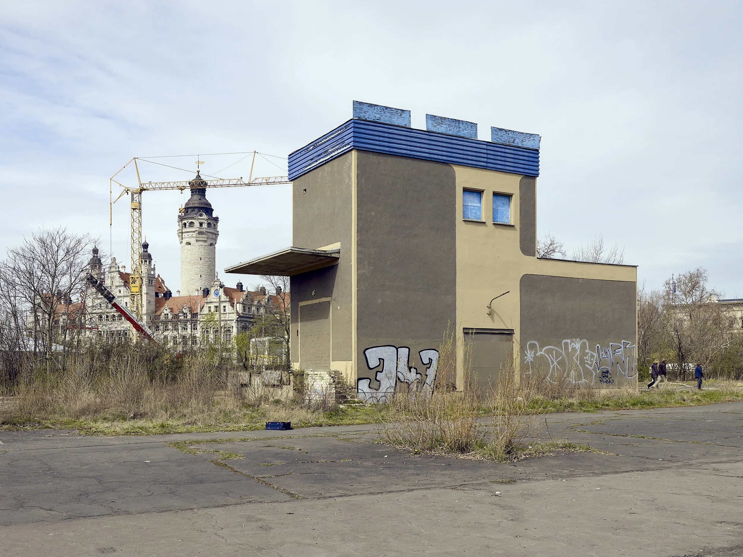 Verfallenes Gebäude mit Graffiti, im Hintergrund eine Baustelle mit Kran und eine Burg mit Türmen