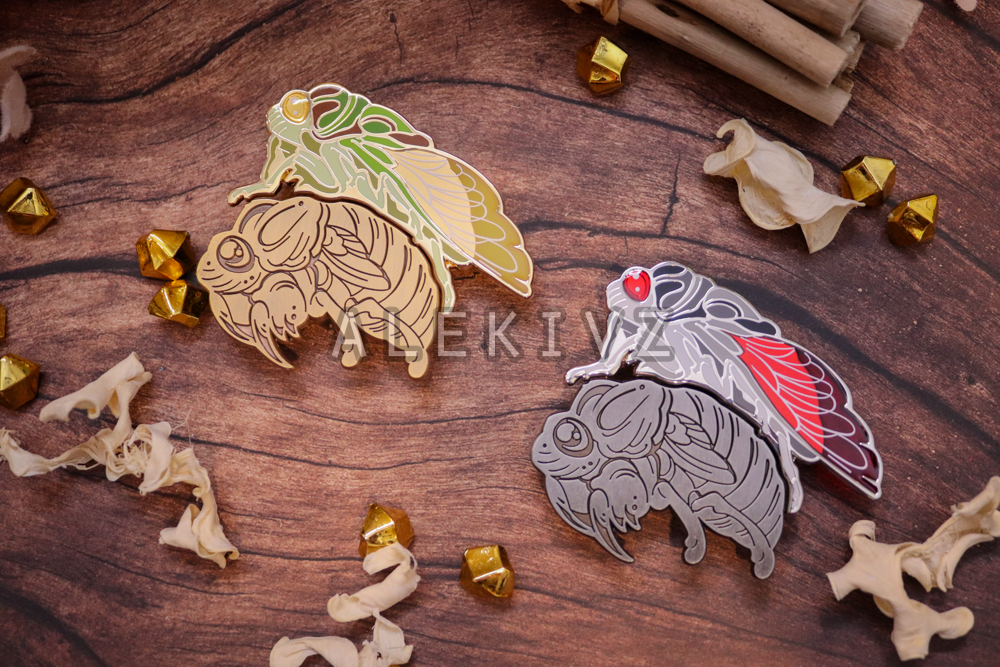 Enamel pin design example of a matching pin set. Features two cicadas, a nymph/shell and emerged adult. Nymph is entirely antique metal with recessed details, while the adult is a full hard enamel pin with layered translucent enamel and screenprintin