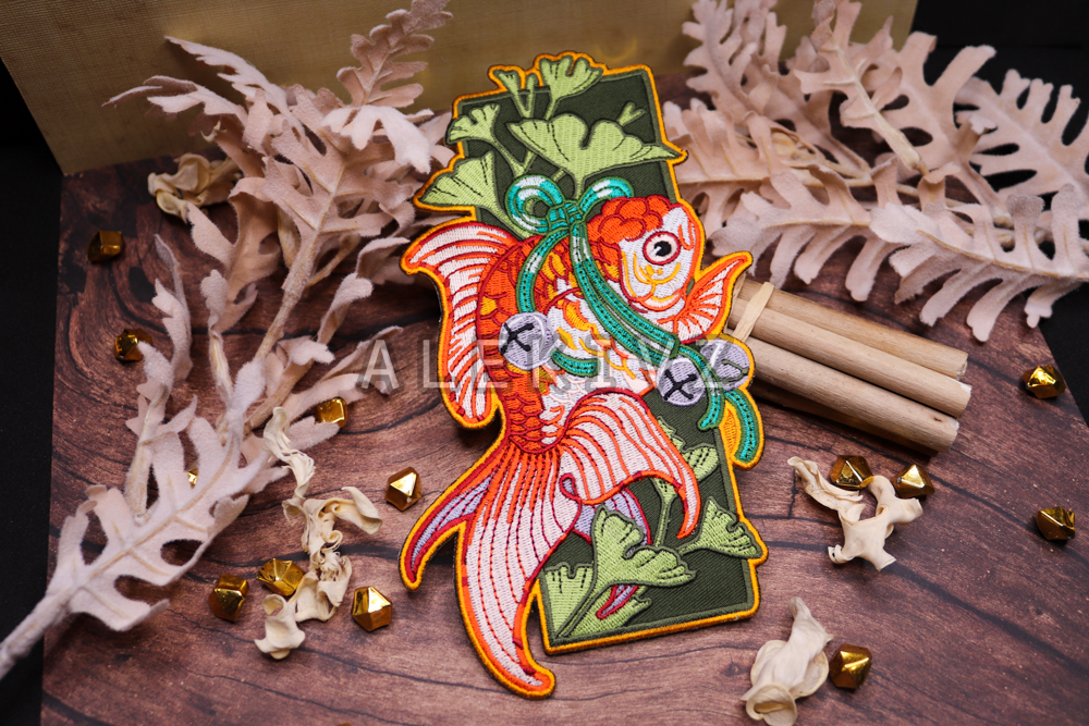 Example of embroidered patch design of a goldfish with gingko and bells. Features embroidered details in a variety of techniques.