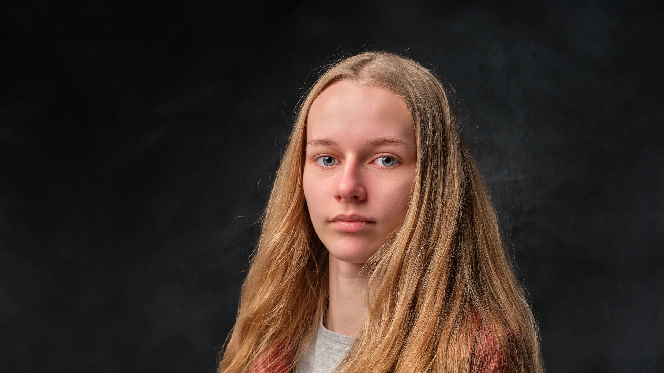 Portrait of a young woman with long blonde hair and blue eyes against a black background.