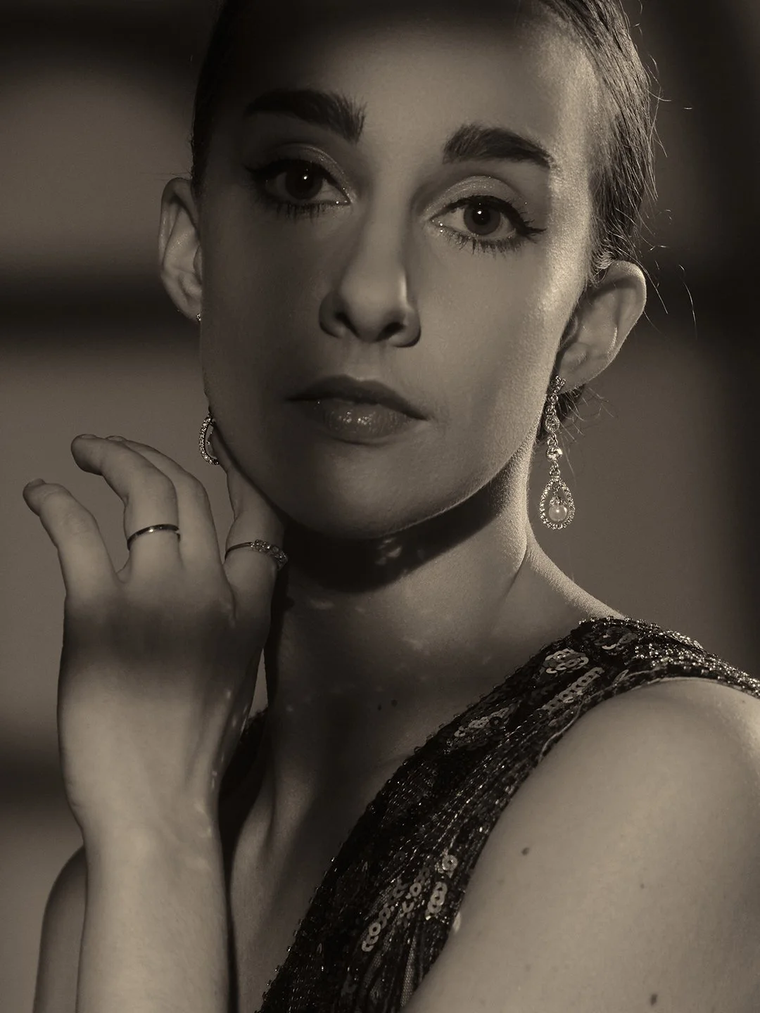 A close-up, head-on studio portrait of a person with a bold, alternative aesthetic. They have vibrant red hair with dark roots and choppy, textured bangs. Their makeup is dramatic, featuring sharp, elongated winged eyeliner, smoky burgundy eyeshadow,