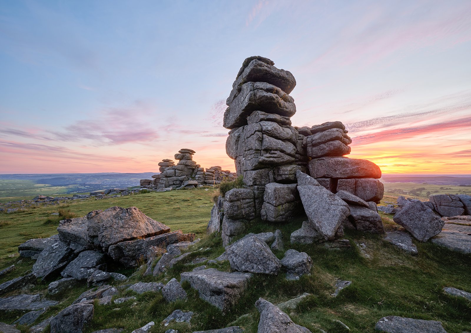 Fine art landscape photograph of Great Staple Tor on Dartmoor at sunset, showing the weathered granite towers illuminated by warm golden hour light against a twilight evening sky.