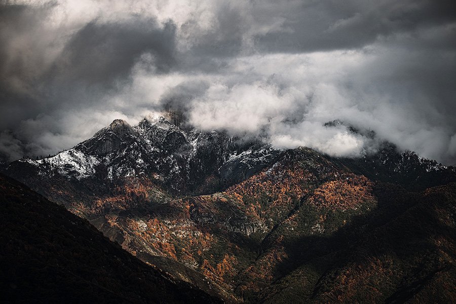 Snow-capped mountain peaks under a cloudy, dark sky with visible mist and fog.