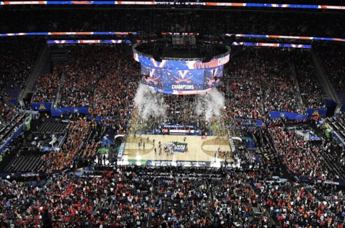Crowd celebrating on a basketball court after winning a championship, with confetti and a large screen displaying 'CHAMPIONS' in the background.