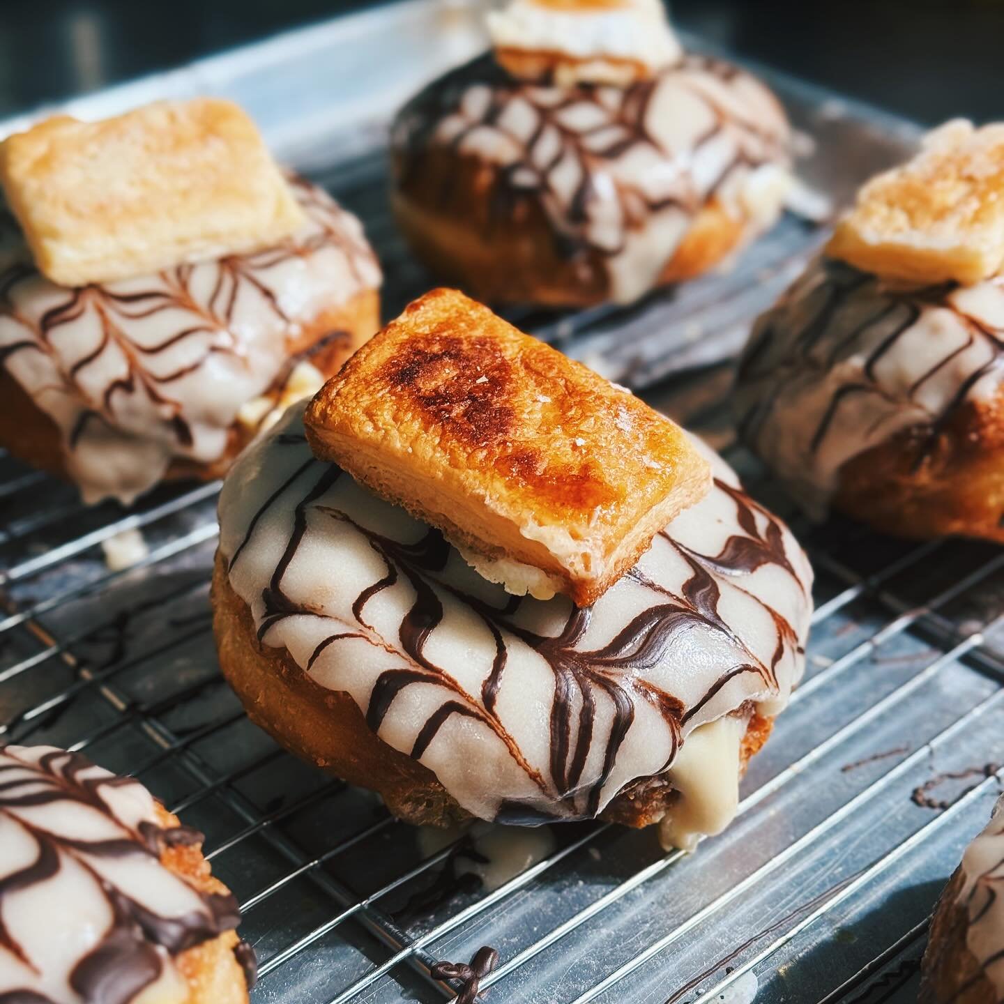 Have you spotted this beauty in our cabinets yet? 👀 It&rsquo;s our delightful Custard Slice Donut Hybrid, with a hint of passion fruit to keep the summer vibes alive☀️Creamy vanilla custard and passion fruit filling, coated with a crispy vanilla gla