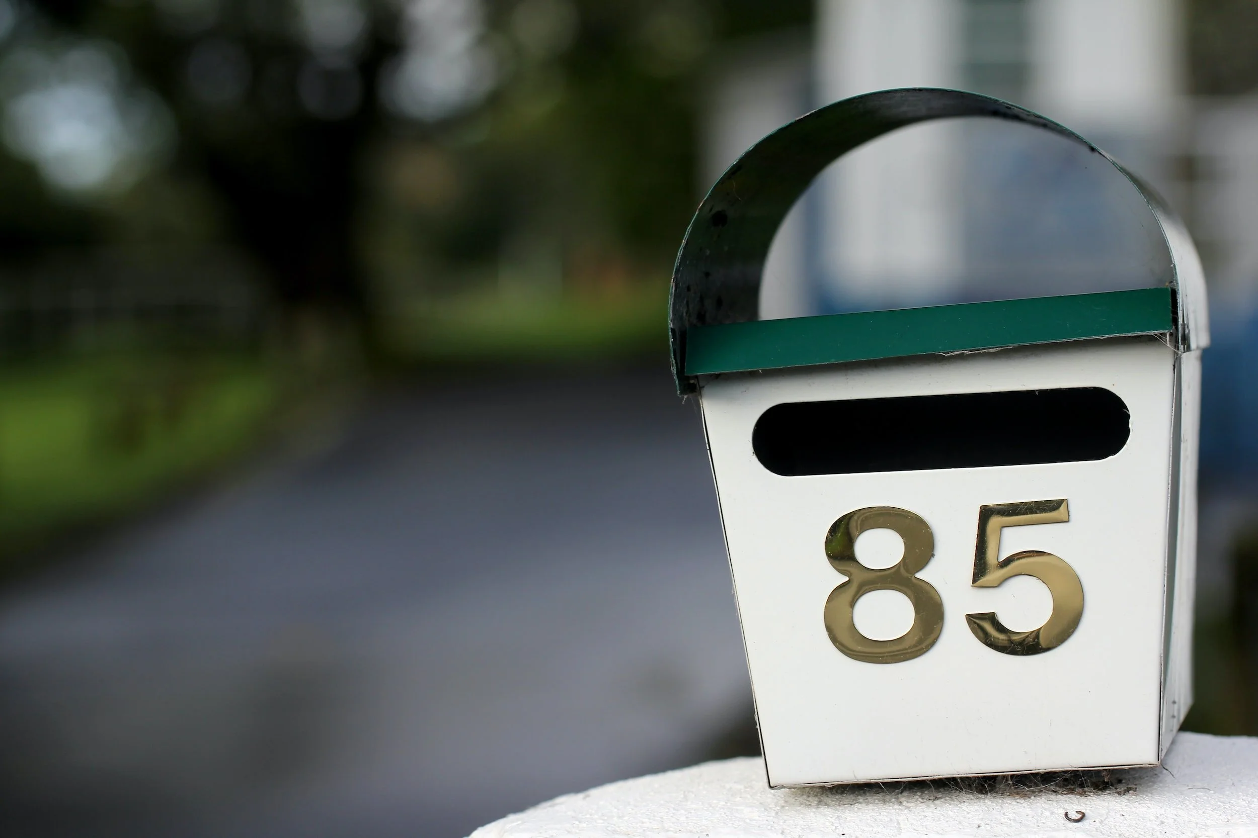 Close-up of a white mailbox with the number 85 in gold, on a chair with a green stripe on the top.