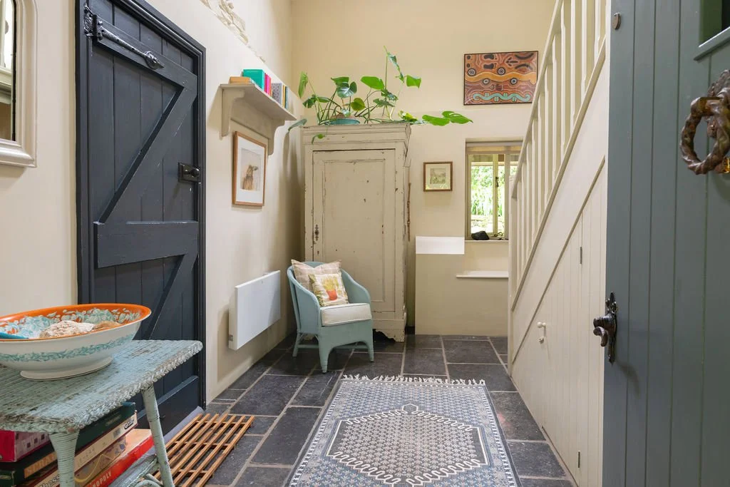 Entryway with a black barn door, a white cabinet, a small armchair with a cushion, framed artwork, a window, and a gray and white patterned rug on dark stone flooring.