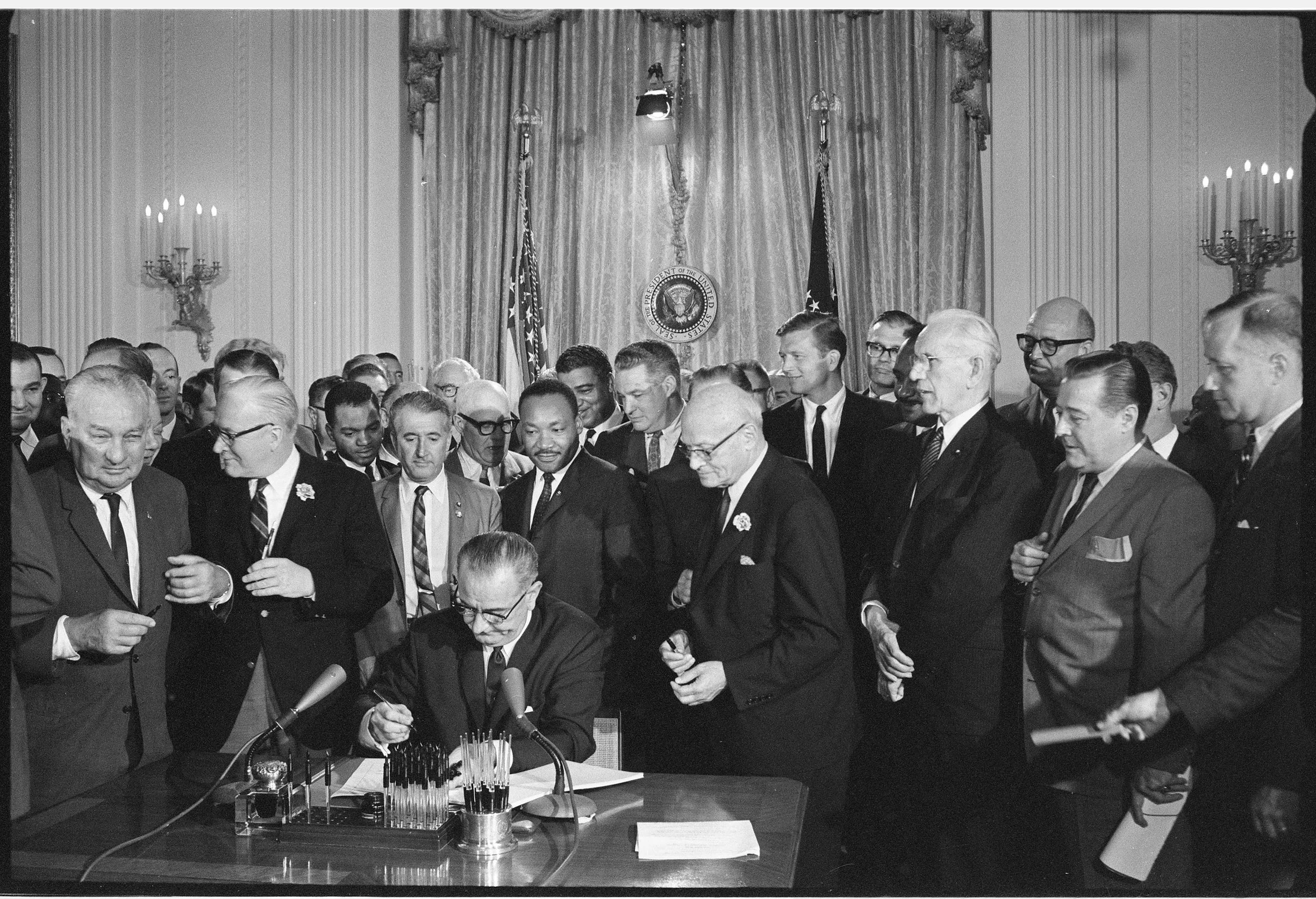 President Johnson signing the Civil Rights Act on July 2, 1964 in the Oval Office surrounded by Congressmen.