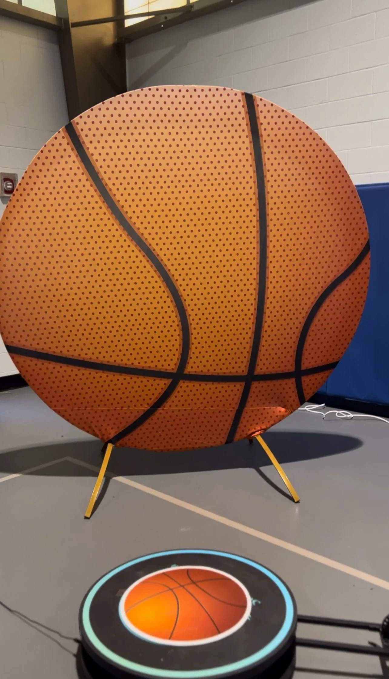 A large, round, basketball-themed inflatable object on a stand, with a smaller basketball graphic projected onto the floor in front of it.