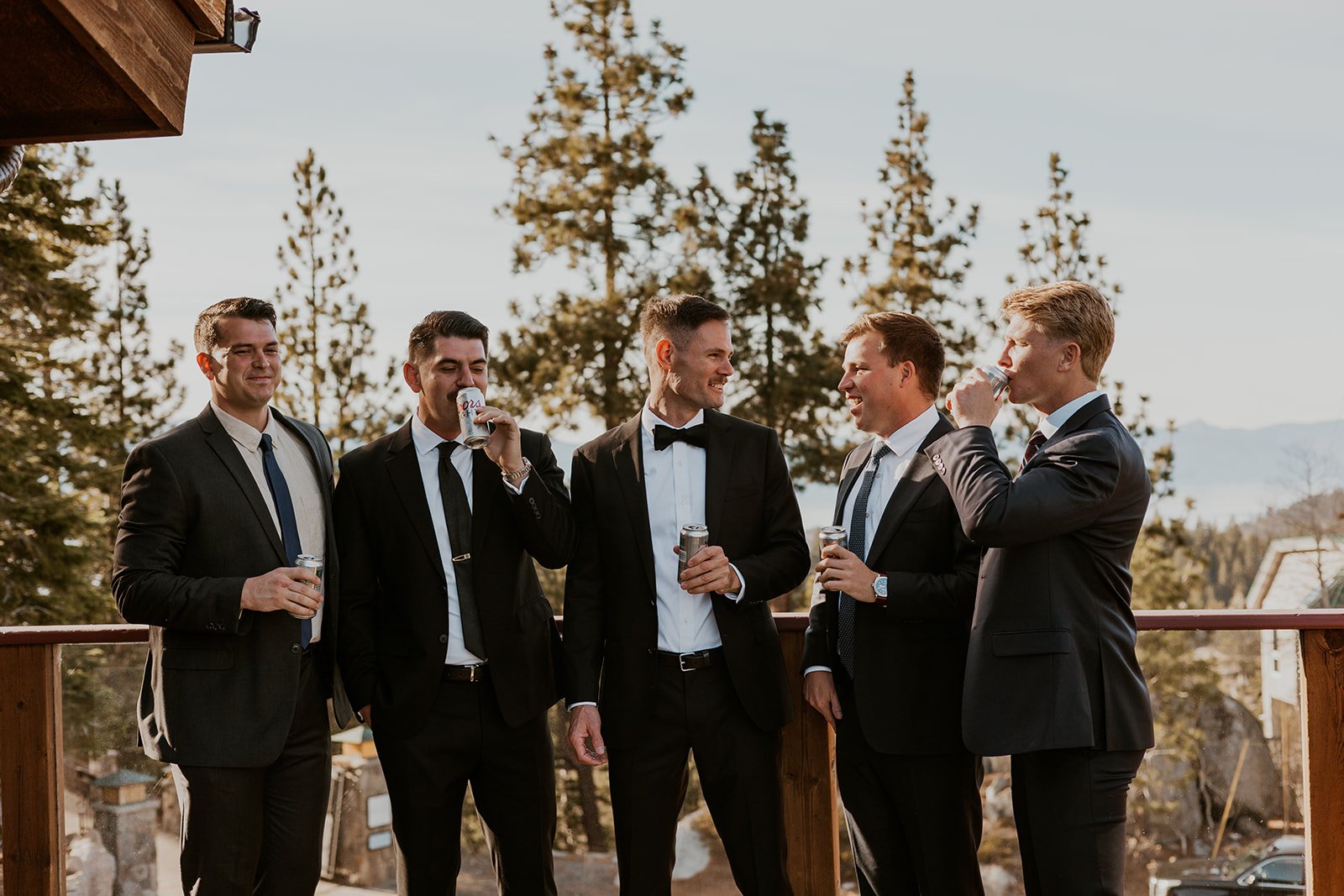 A groom and his groomsmen wearing their suits and standing on a balcony at Tahoe Blue Estate smiling and sipping on their beers.