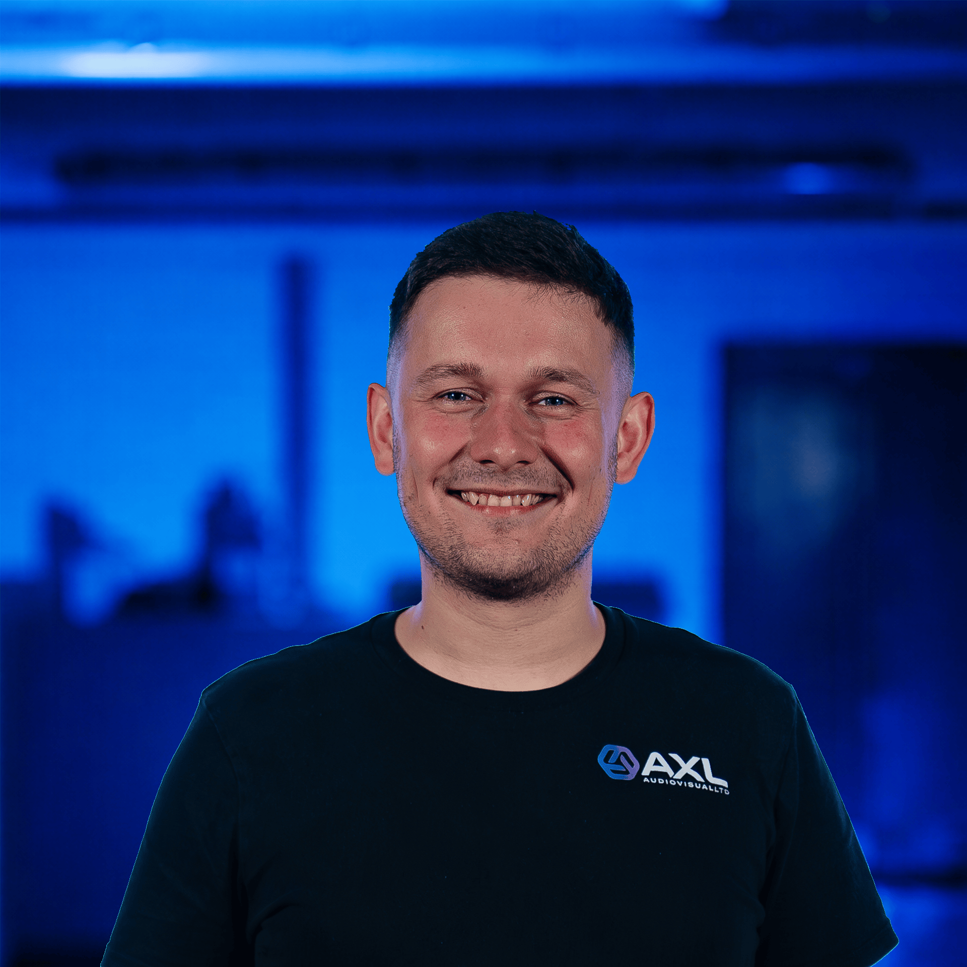 A young man standing on a stage with colorful lights and a large screen in the background. 
