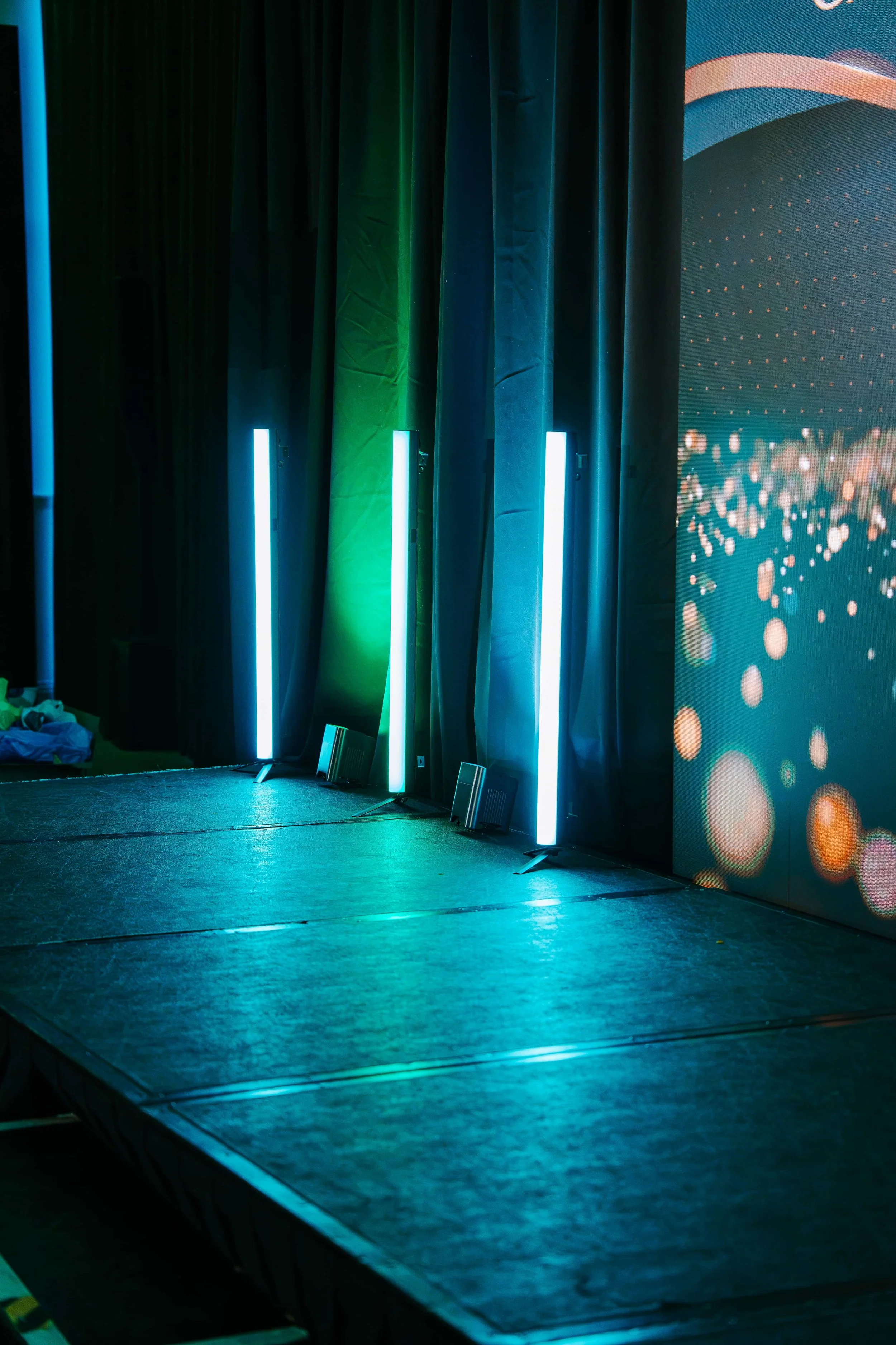 Wireless LED tubes and uplighters in teal and green across the stage front, beside the edge of the LED wall