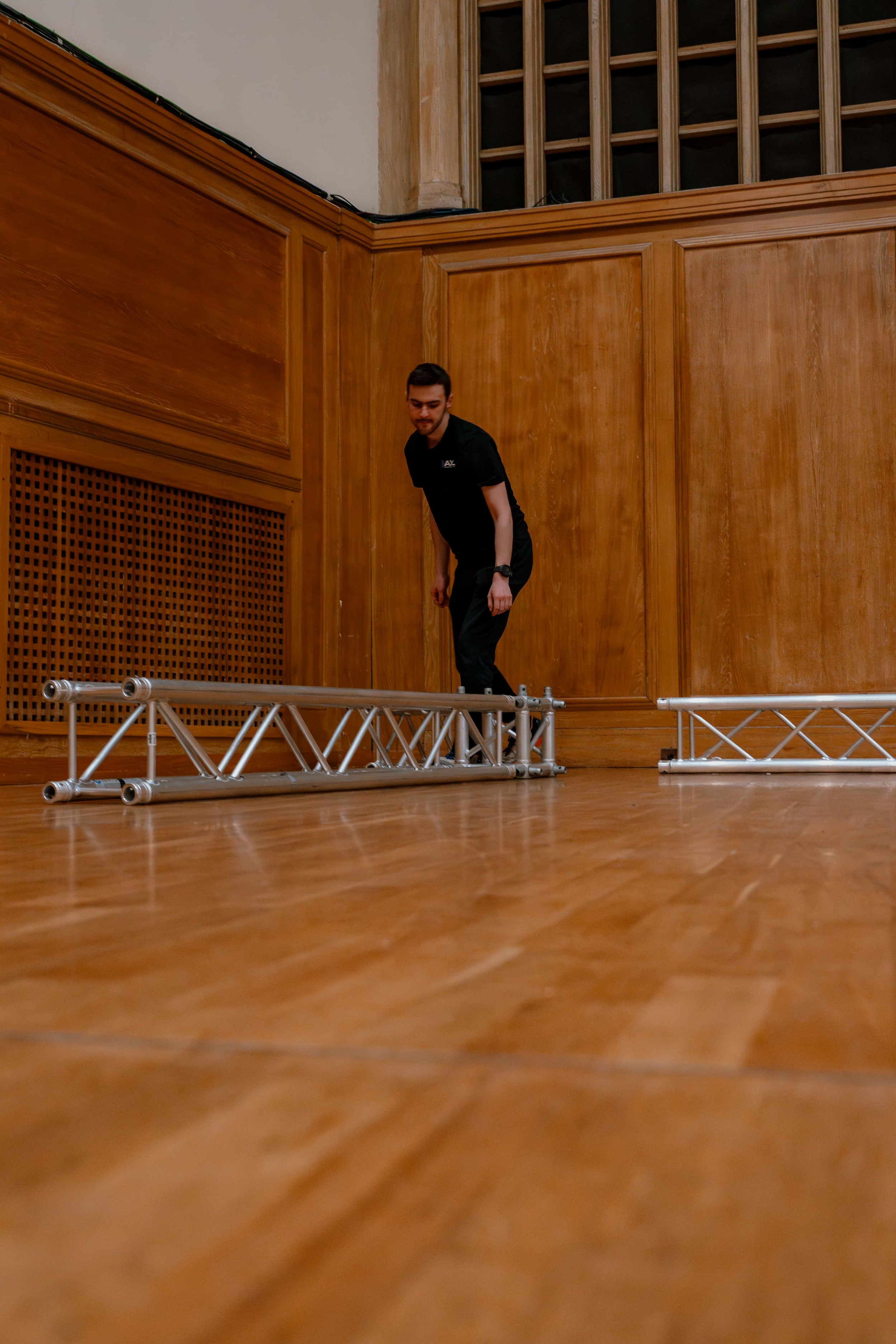Square truss laid out on the floor of a wood-panelled hall during an AV get-in