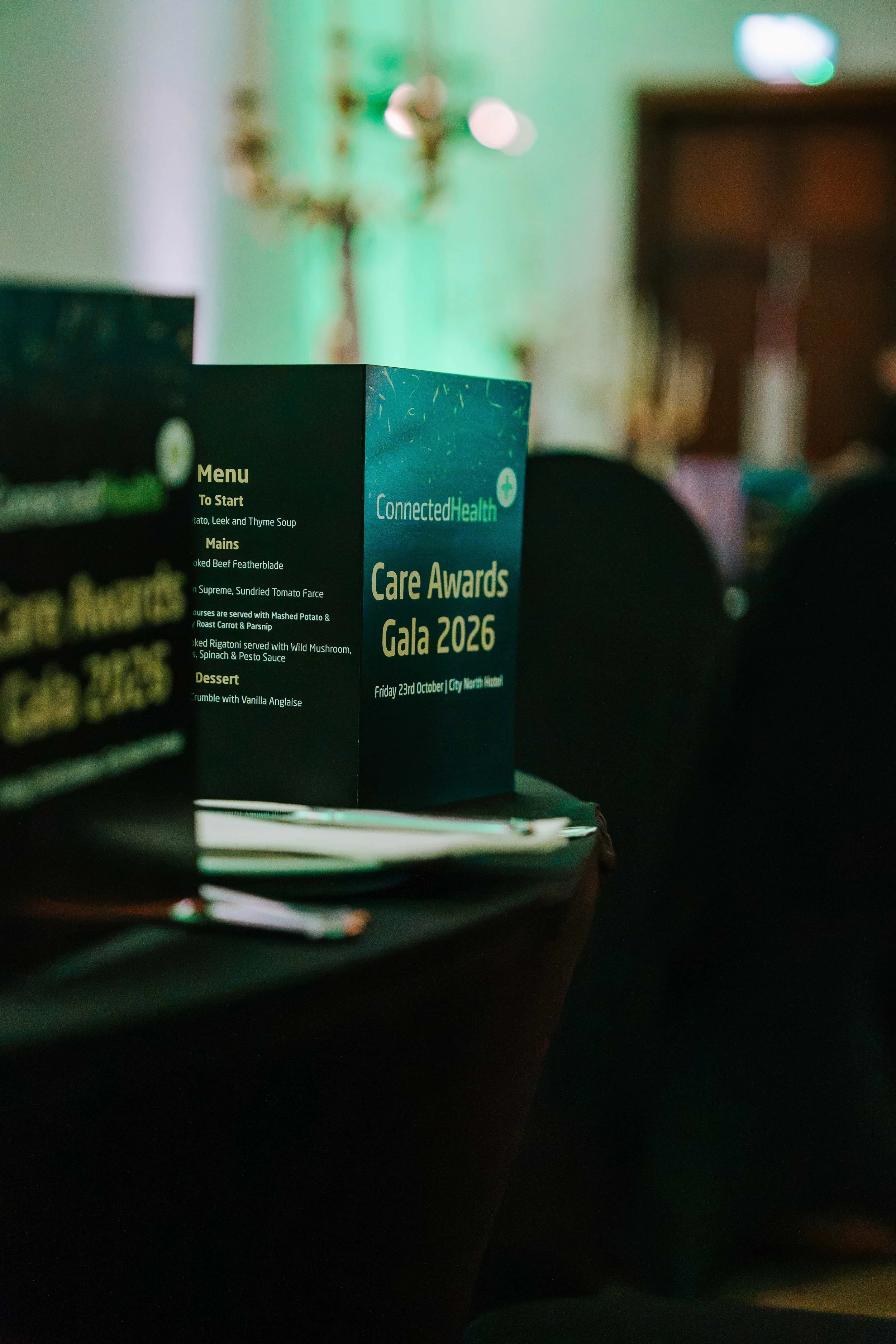 Connected Health Care Awards Gala 2026 menu card on a black table, with green uplighting and a candelabra behind