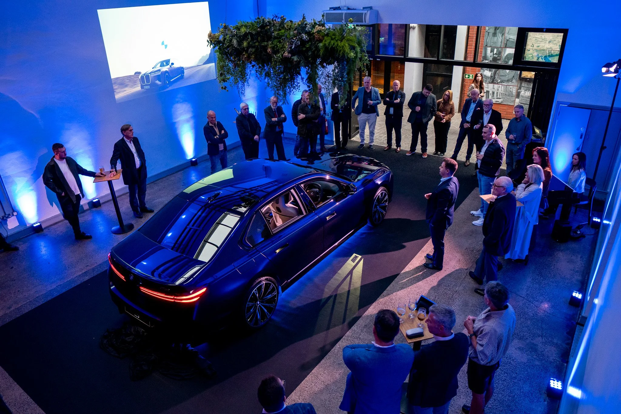 Guests gathered around the newly unveiled BMW i7 under blue uplighting at Waterman House, Belfast