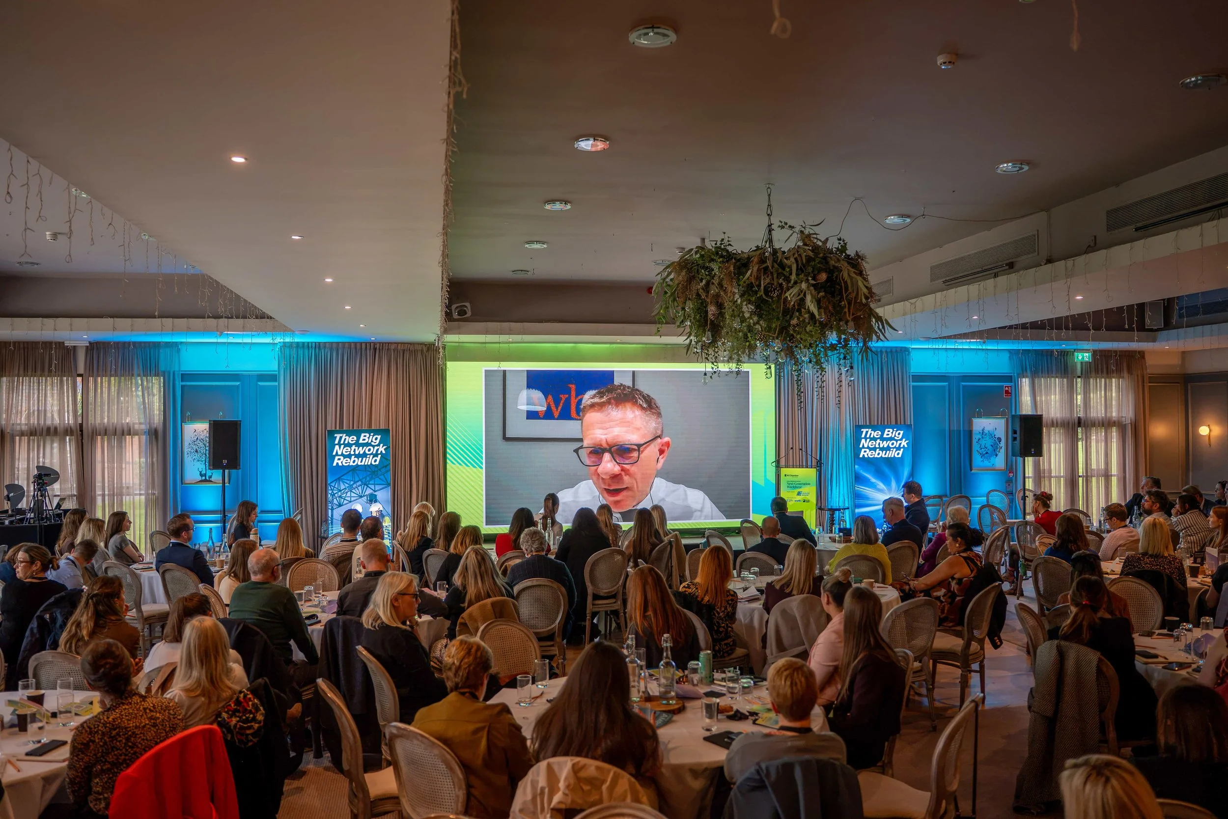 Wide view of a full conference room with a remote speaker on the LED wall and a camera at the back of the room